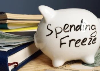 White piggy bank on top of a desk with the words: Spending Freeze written on it.