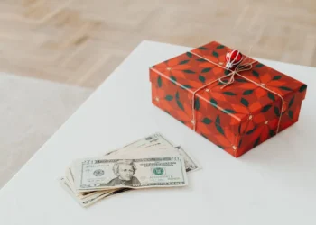 A pile of American dollar bills and a wrapped gift sit on a white table. A holiday loan may just put you more in debt.