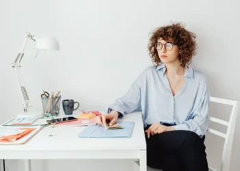 Woman wearing glasses holds a pile of money and sits at a table. Money dysmorphia is a distortion of your financial situation.