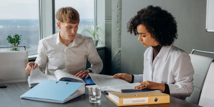 Two colleagues in white shirts sit at a desk looking at papers. A financial therapist can be an excellent option to get you on track, or back on track.