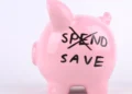 A pink piggy bank with the word SPEND crossed out and SAVE written instead. Perfect for no-buy challenges.