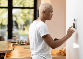 Man in white shirt sets his thermostat. Installing a smart thermostat is one of the DIY projects that can save you money.
