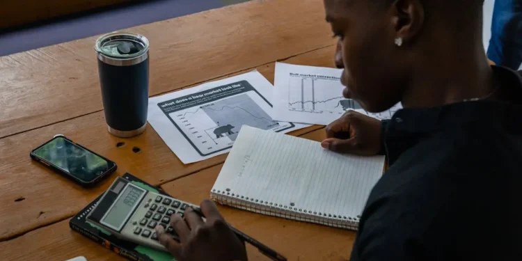 Man sits at a table working on a calculator to figure out his cost of living number.