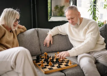 A senior couple sits on a couch playing chess. Planning ahead for retirement expenses can save you money and peace of mind.