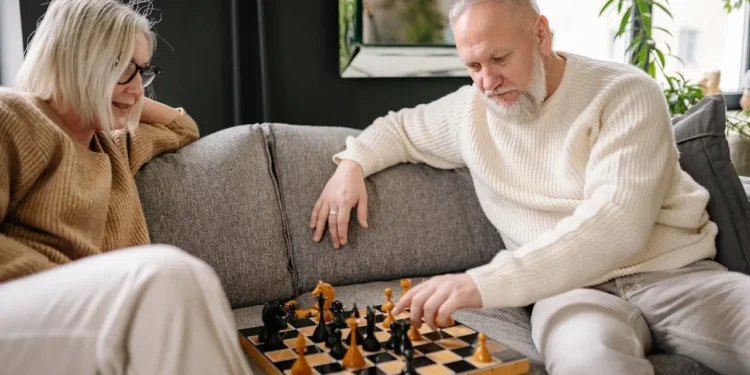 A senior couple sits on a couch playing chess. Planning ahead for retirement expenses can save you money and peace of mind.