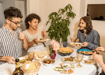 Group of people sit around a table covered in food. Making potluck dinners can help a lower budget.