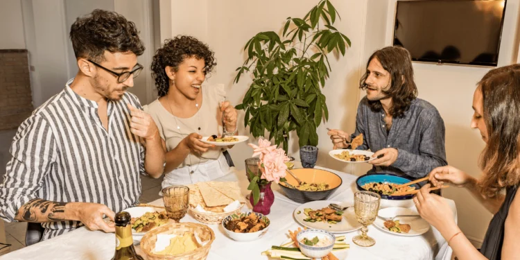 Group of people sit around a table covered in food. Making potluck dinners can help a lower budget.