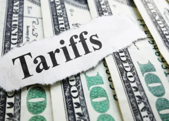 A paper that says 'tariffs' on a pile of US $100 bills