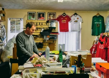 Man stands in a very cluttered room. A side effect of buying stuff you don't need is clutter.