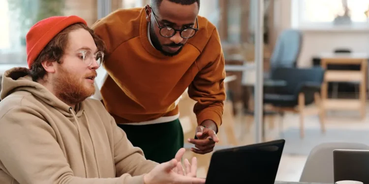 Two young men look at a laptop together. Wealth and poverty mindsets in your 20s.