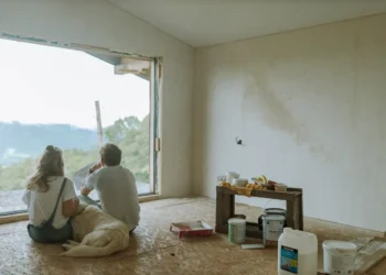 Two people sit with their dog in a dilapidated house. Reno costs are one of the most common home buyer regrets.