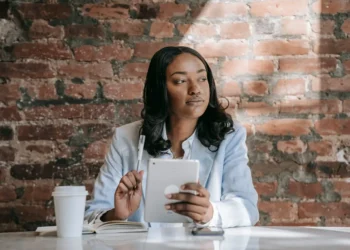 Woman sits at a table reading on a tablet. Reading daily is one of the habits of Warren Buffett.