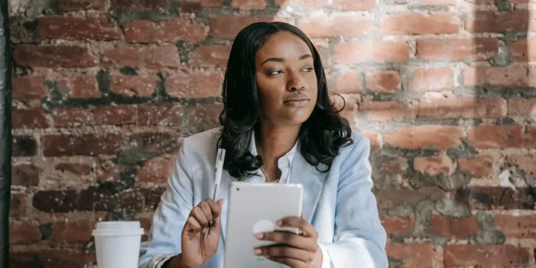 Woman sits at a table reading on a tablet. Reading daily is one of the habits of Warren Buffett.