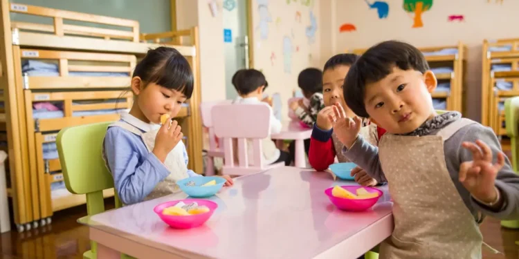 Group of young kids eats snacks at a daycare. Childcare costs are on the rise.
