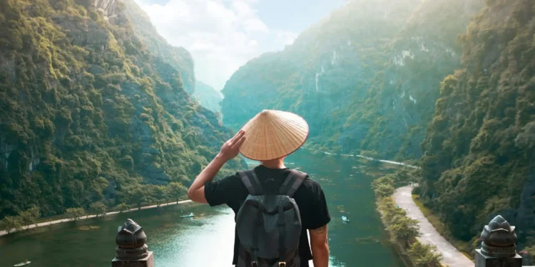 Man with bamboo hat stands in front of beautiful landscape. Moving abroad demands deep thinking first.