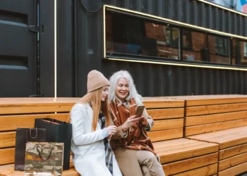 Two women sit on a bench together looking at a phone. Knowing your money personality can help you nail your finances.
