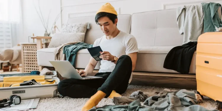 Man sits on floor booking travel with a laptop.