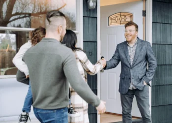 A man meets a family at the door of a house. Getting real estate agent advice is helpful.