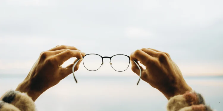 Two hands hold up a pair of glasses. Are you a victim of framing bias?