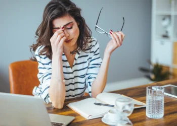 Woman sits at desk, pinching her nose. These are the three most asked questions about financial stress.