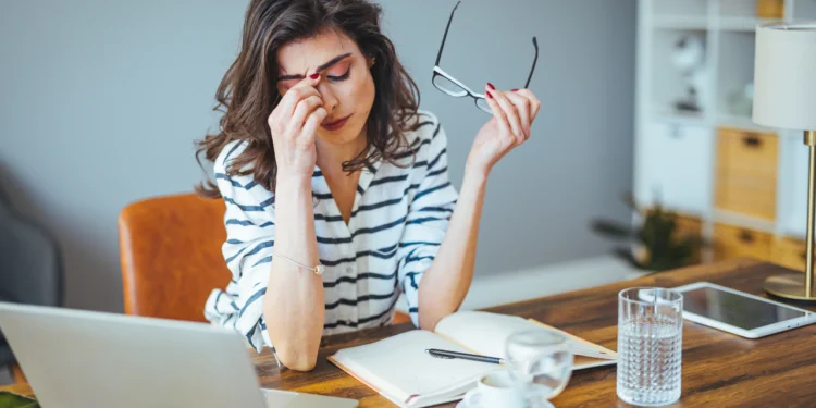 Woman sits at desk, pinching her nose. These are the three most asked questions about financial stress.