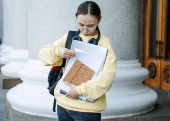A young woman holds books in her arms, looking at a piece of paper. How do student loans affect your credit score?