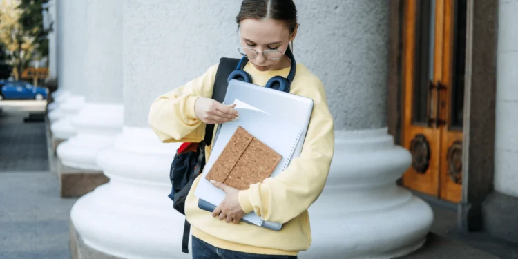 A young woman holds books in her arms, looking at a piece of paper. How do student loans affect your credit score?