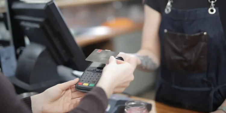 Person holds up their card to pay at a kiosk. Tipping culture is an important topic.
