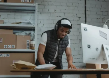 Man wearing a hat and headphones works at a desk. Selling online is one of the great side hustles for introverts.