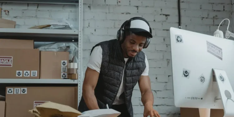Man wearing a hat and headphones works at a desk. Selling online is one of the great side hustles for introverts.