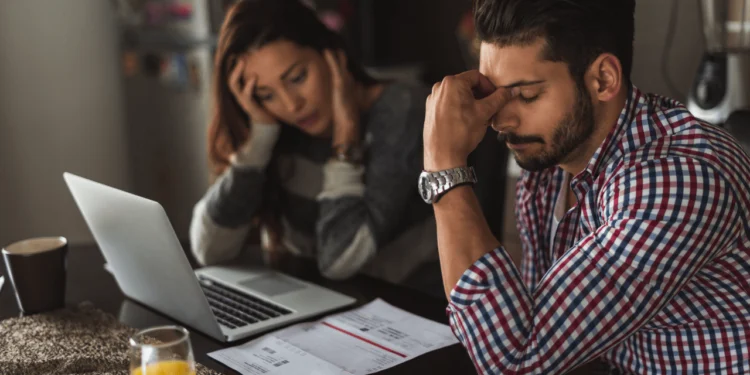 A man and woman look worried while looking at an open laptop. Money insecurity can be crippling.