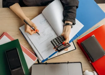 Person holds calculator in one hand and writes in a book in the other. Having a budget sets your intent.