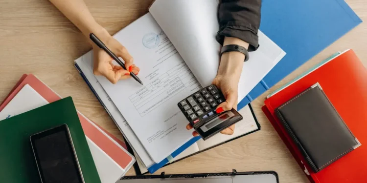 Person holds calculator in one hand and writes in a book in the other. Having a budget sets your intent.