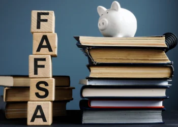 White piggy bank on top of stack of books beside blocks spelling out FAFSA.