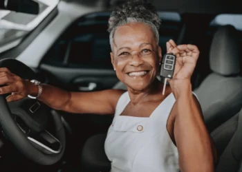An older woman sits in a car holding up keys - buying a used car takes some planning.