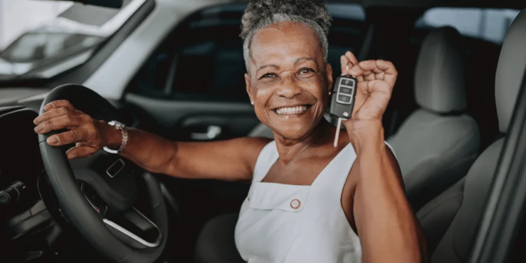 An older woman sits in a car holding up keys - buying a used car takes some planning.