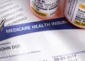 A bottle of prescription pills sits on top of paper with Medicare facts.