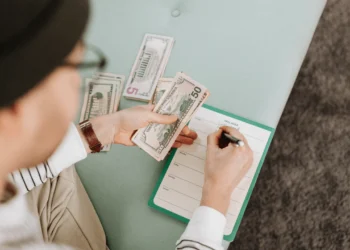 Man practices frugal living by counting dollar bills while writing in a notebook.