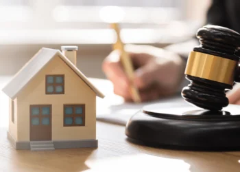 A tiny house sits on a desk with a gavel. Foreclosure looks different depending on what side you're on.