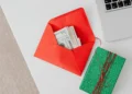 Orange envelope filled with cash beside a green festive gift box.