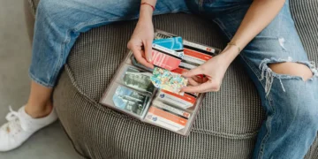 Person sits on chair, holding wallet full of colorful gift cards.