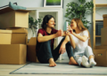 Man and woman sit on floor amid moving boxes.