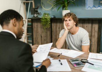Overwhelmed man sits across desk from financial advisor.